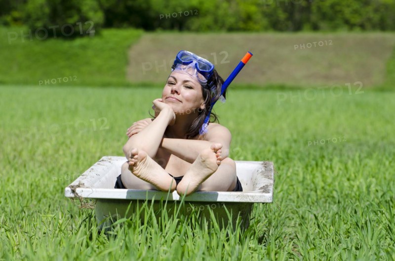 Woman Sitting in a Bathtub on a Green Field with Grass and a Diving Mask in a Sunny Day