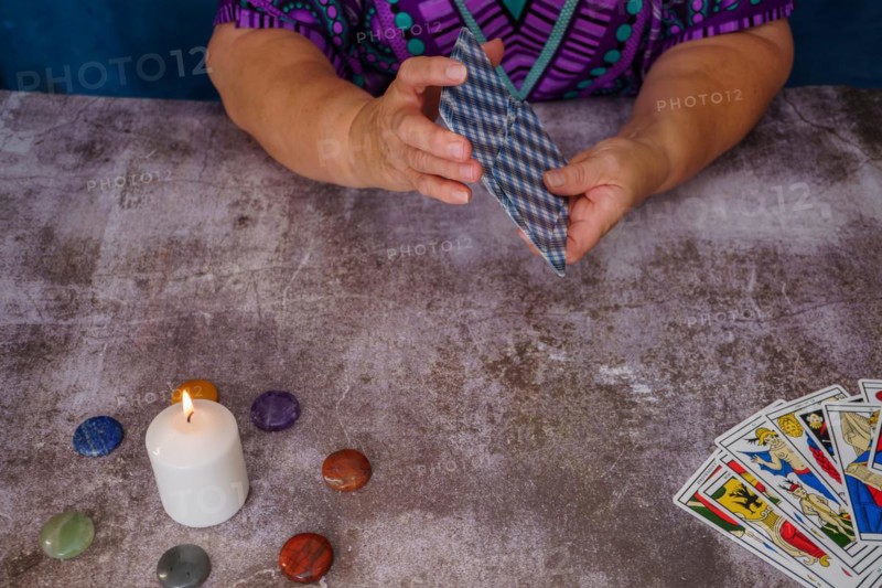 Woman shuffling tarot cards on a table with candles and chakra stones