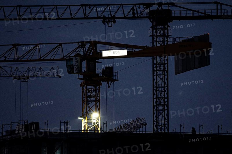 A worker draws on scaffolding and in front of a crane on a newly built house