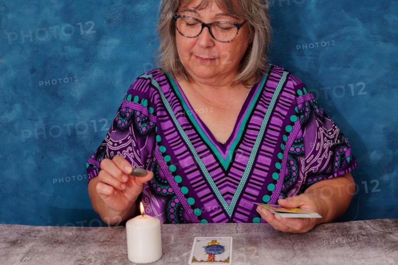 Elderly fortune teller woman with white hair casting tarot cards concentrating on a white candle