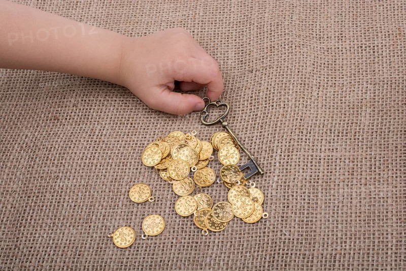 Hand holding a retro styled key over fake gold coins