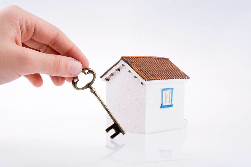 Hand holding a golden key near a house on a white background