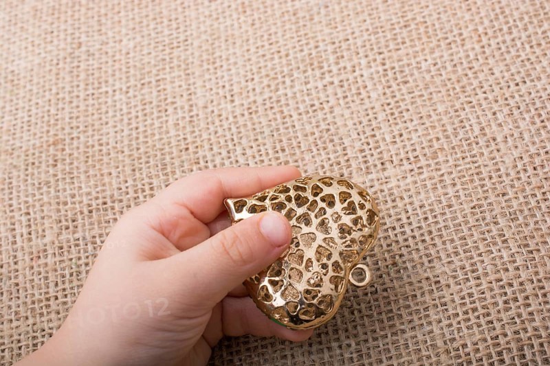 Heart shaped gold color metal object in hand