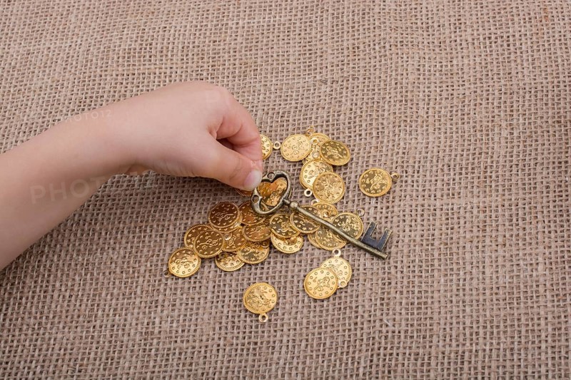 Hand holding a retro styled key over fake gold coins