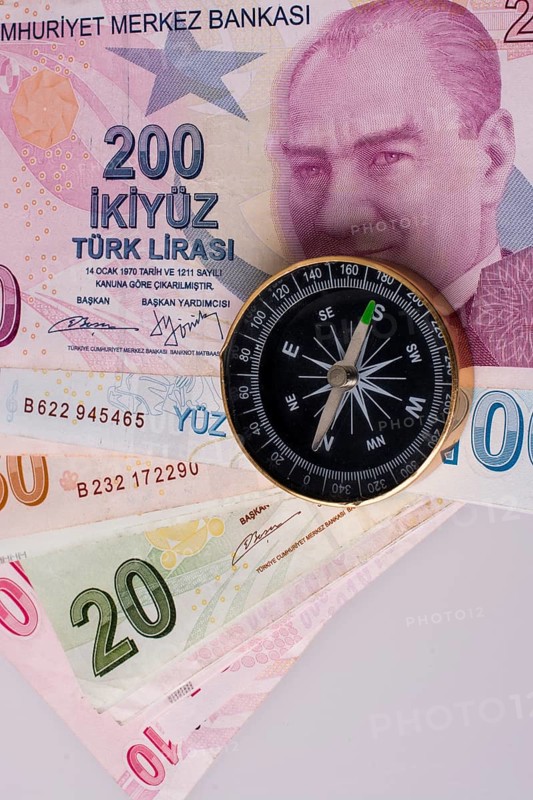 Turkish Lira banknotes by the side of a compass on white background