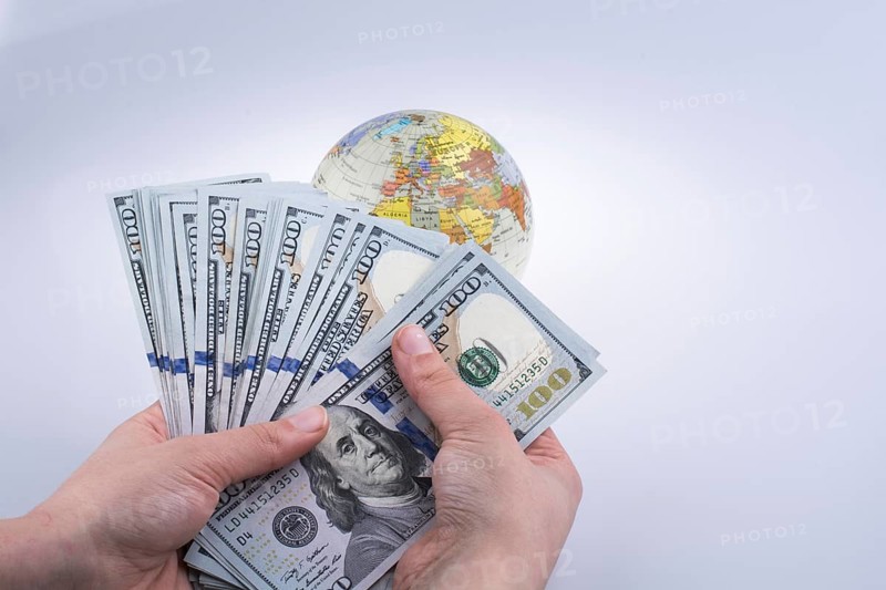 Human hand holding American dollar banknotes by the side of a model globe on white background