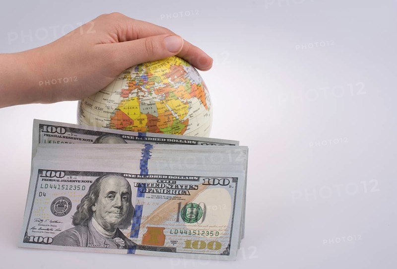 Human hand holding a model globe by the side of aAmerican dollar banknotes on white background