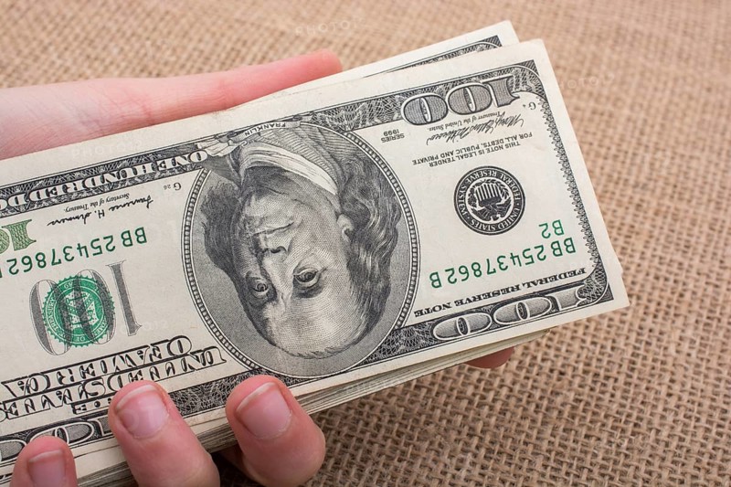 Hand holding banknote bundle of US dollar on a linen canvas background