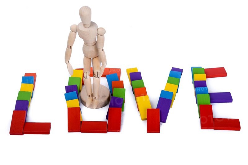 Wooden puppet standing amoung colorful dominos which write love