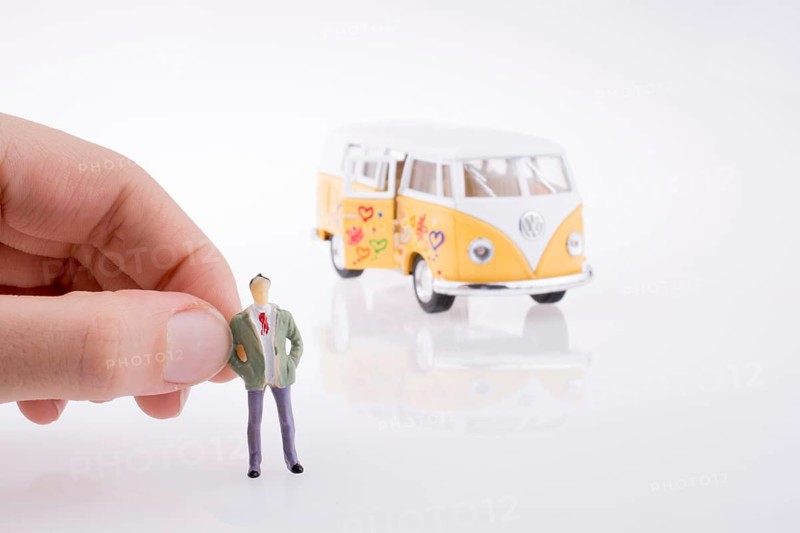 Hand holding a human figure near a peace van on a white background