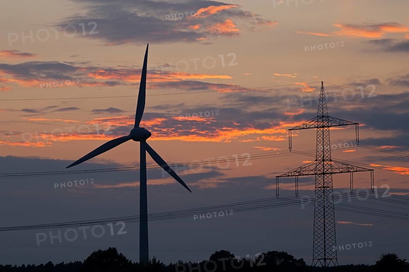 Wind power station and high voltage pylon in front of evening sky