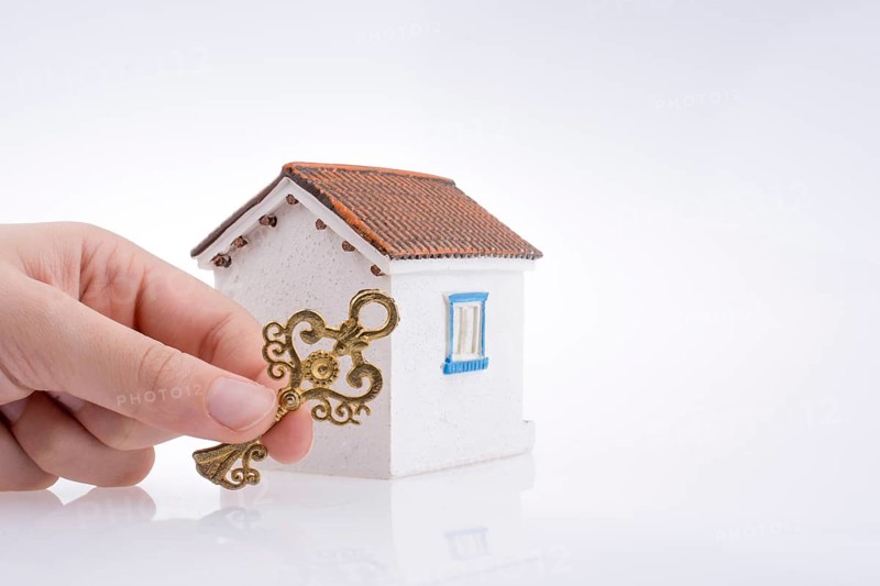 Hand holding a golden key near a house on a white background