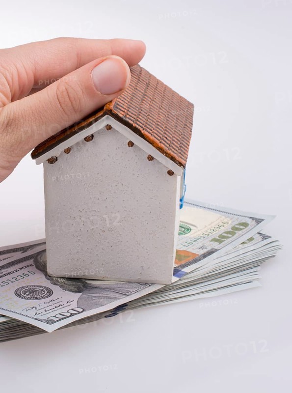 Hand holding a model house by the side of Turkish Lira banknotes on white background
