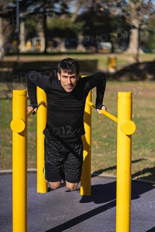 Fit young man doing push ups on horizontal bar outdoors