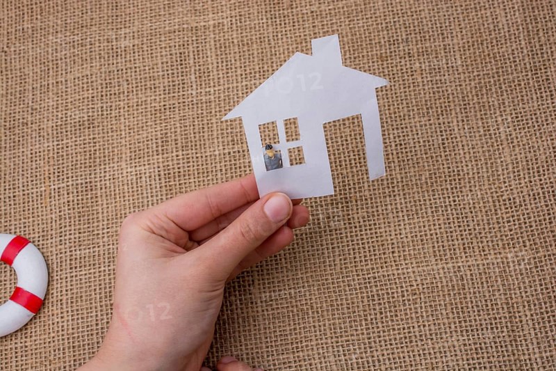 Paper house and a man figurine on a linen canvas background