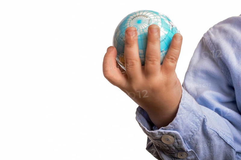 Baby with blue shirt holding a small globe in hand on white background