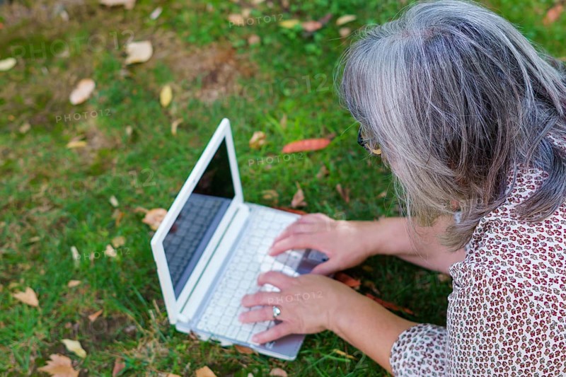 Top view of a white-haired woman working on her laptop computer lying on the grass in a park