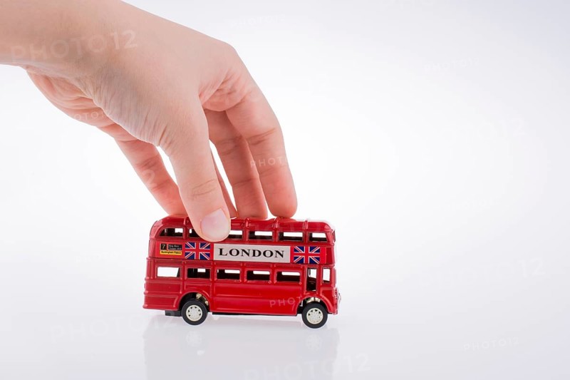 Child hand playing with London double decker bus model on white background