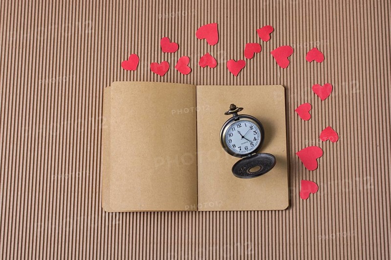 Retro Pocket watch on notebook with red paper hearts around