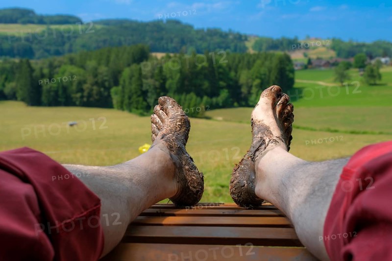 Feet of a man on a wooden lounger at the Wuppenau barefoot path on the Nollen