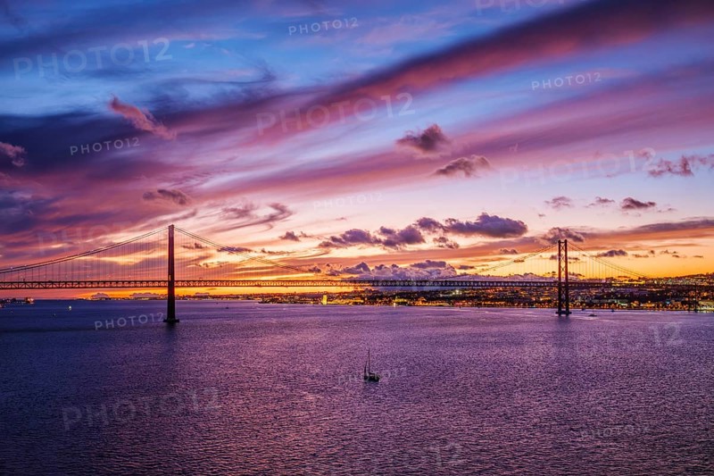 View of 25 de Abril Bridge famous tourist landmark of Lisbon connecting Lisboa and Almada on Setubal Peninsula over Tagus river in the evening twilight with boats. Lisbon