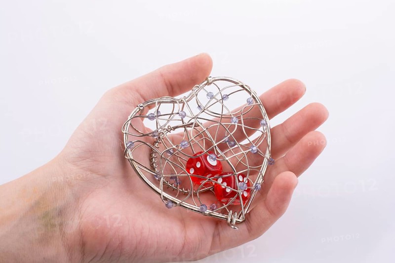Hand holding Red dice in a heart shaped cage on a white background