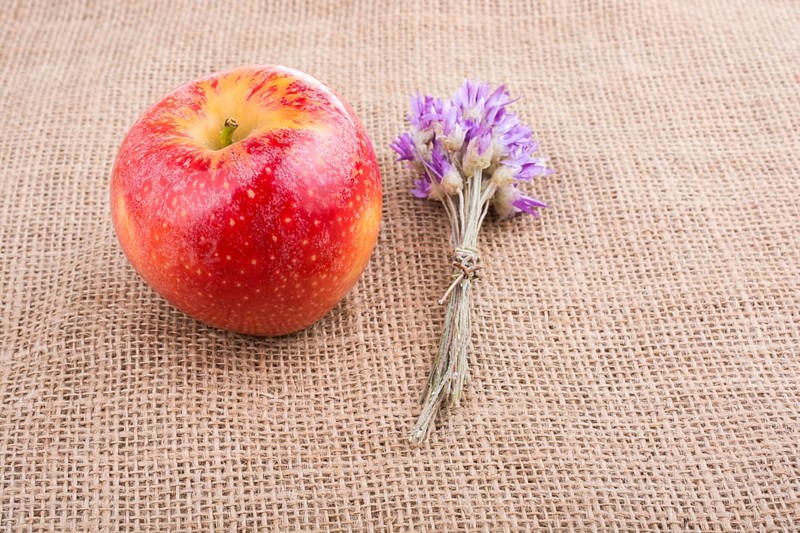 Tiny flower bouquet beside an apple on canvas