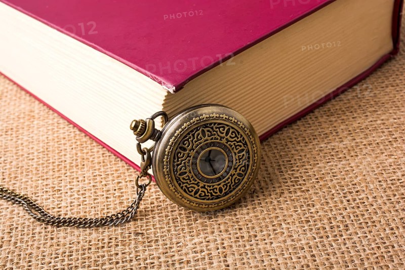 Retro style pocket watch beside a book on a canvas