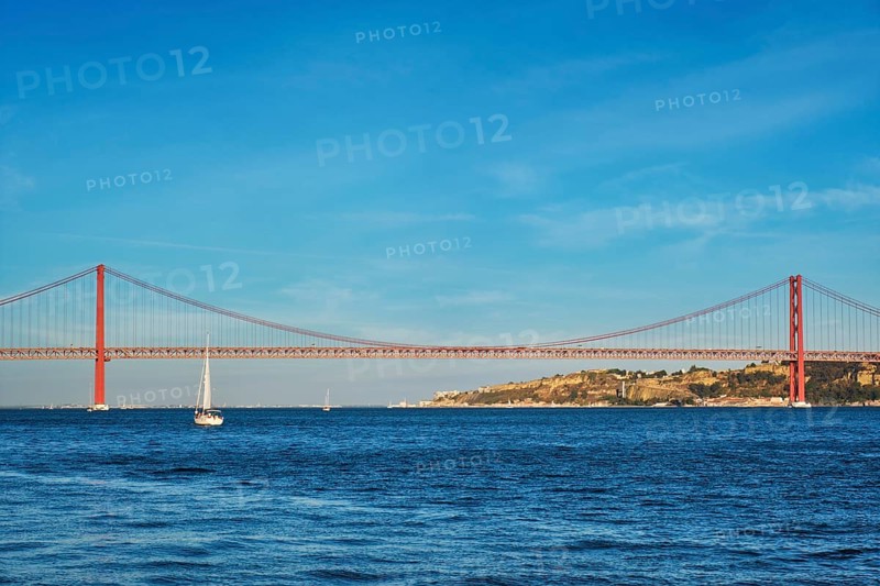 View of 25 de Abril Bridge famous tourist landmark over Tagus river and a tourist yacht boat at sunset. Lisbon