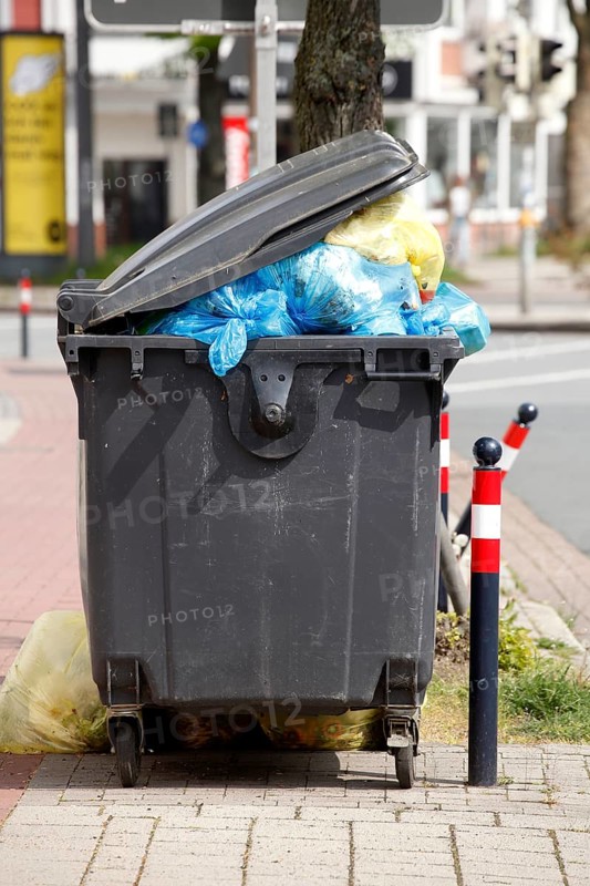 Filled rubbish container with open flap standing by the road