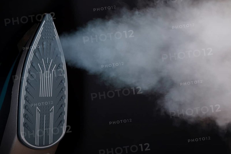 Iron seen from the front with steam coming out of its orifices on a black background