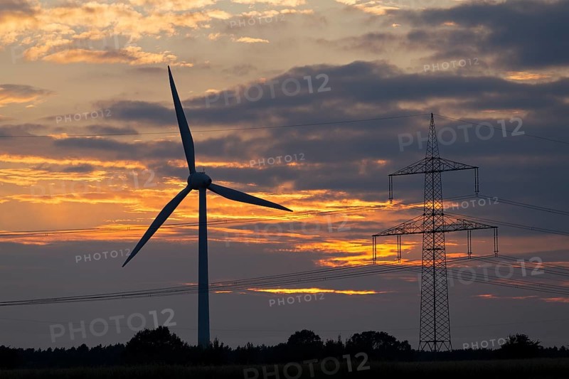 Wind power station and high voltage pylon in front of evening sky