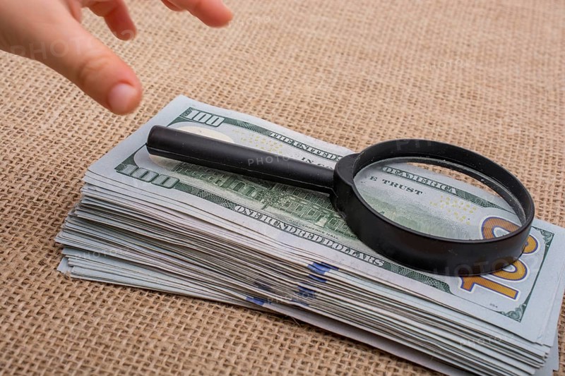 Toddler holding a magnifying glass over the banknote bundle of US dollar