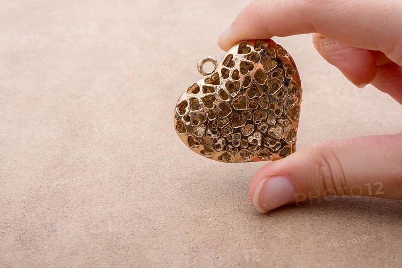 Heart shaped gold color metal object in hand