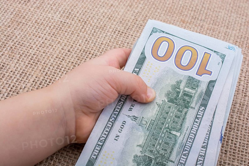 Toddler hand holding banknote bundle of US dollar on a linen canvas background