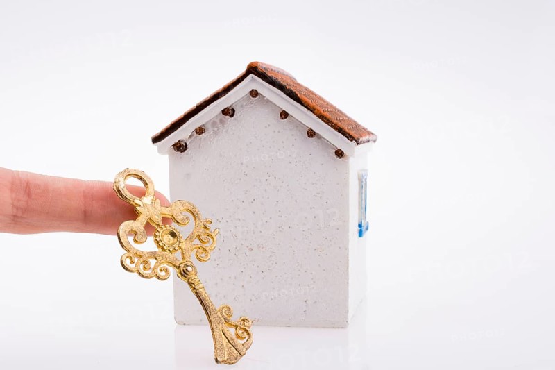 Hand holding a golden key near a house on a white background
