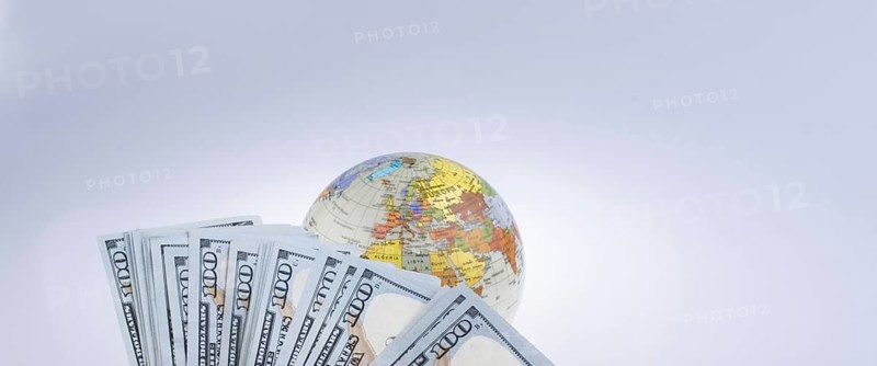 Human hand holding American dollar banknotes by the side of a model globe on white background