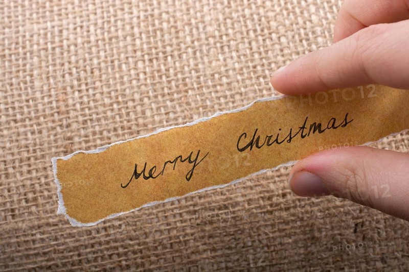 Merry Christmas wording written on a torn paper in hand