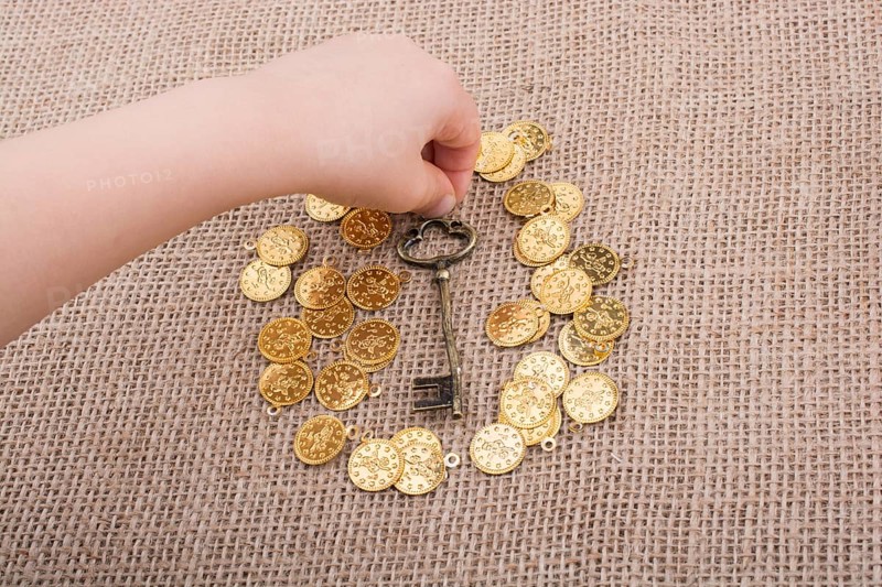 Hand holding a retro styled key over fake gold coins