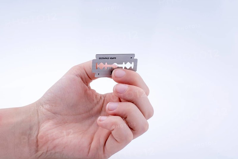 Hand holding a razor blade on a white background