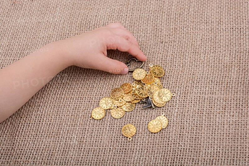 Hand holding a retro styled key over fake gold coins