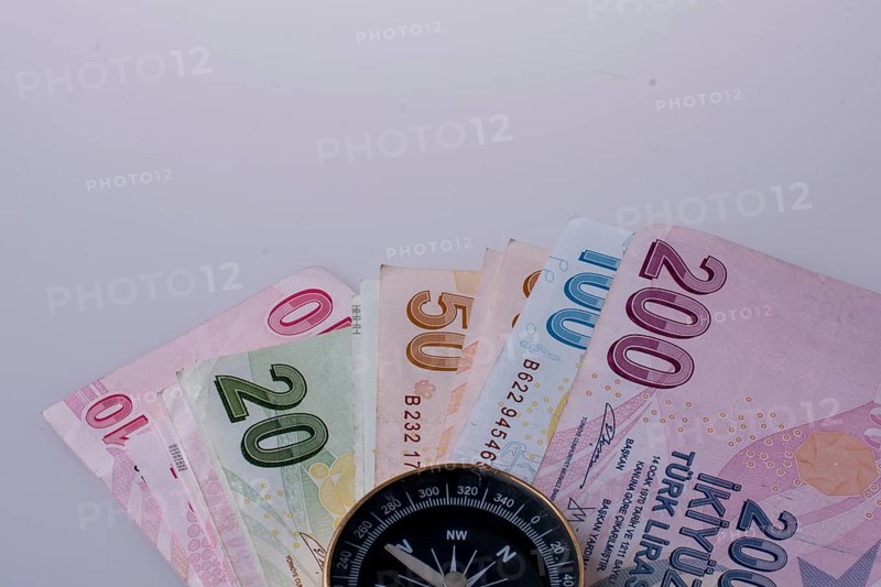 Turkish Lira banknotes by the side of a compass on white background