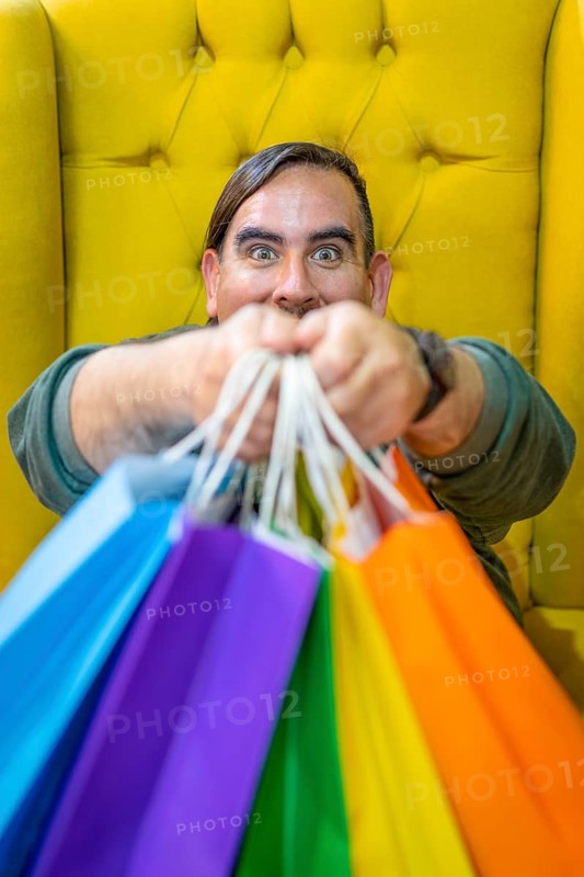 Happy man holding shopping bags on yellow background. Joy of consumption. Purchases