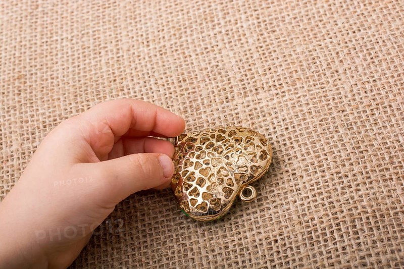Heart shaped gold color metal object in hand