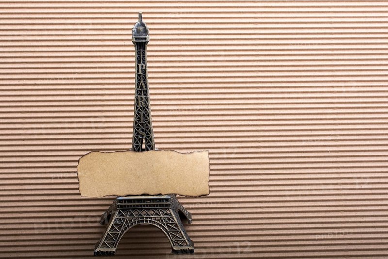 Burnt piece of paper on model Eiffel tower on cardboard
