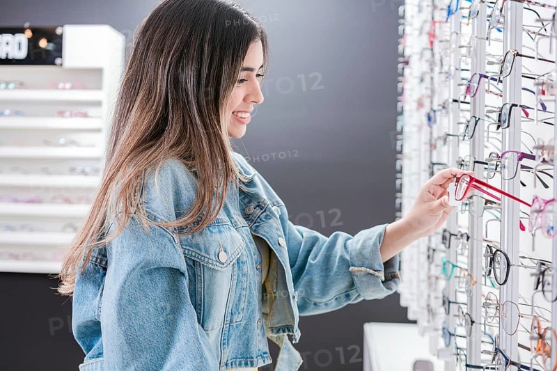 Beautiful girl choosing glasses in an optical store. Young female buyer choosing glasses in an optical store. Customer choosing glasses in an eyewear store