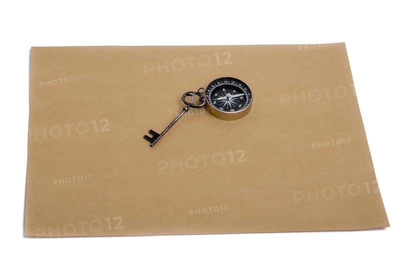 Key and compass on a sheet of colored plain paper with a white background