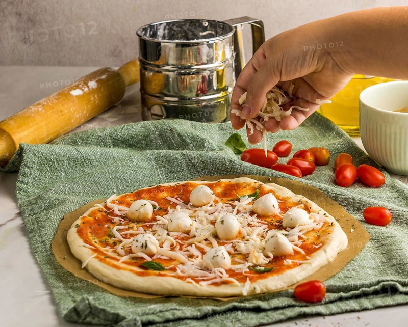 Person sprinkling mozzarella cheese pizza