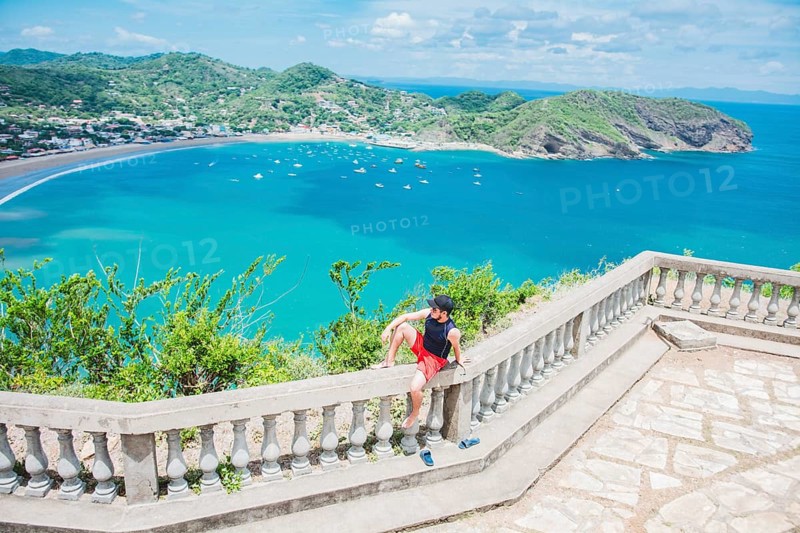 Happy tourist sitting in a viewpoint of a bay. Portrait of tourist man in the view of the bay of San Juan del Sur. Travel and tourism promotion concept