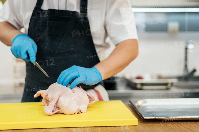 Front view chef with gloves cutting chicken